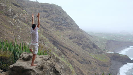 Against-the-picturesque-mountain-ocean-panorama,-a-fit-young-man-harmonizes-meditation-and-exercise-through-sun-salutation-yoga